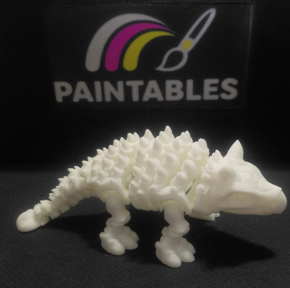 A white 3D printed flexi Ankylosaurus skeleton toy featuring a spiked armored back and a clubbed tail. The articulated model is shown in a standing profile view on a black surface.