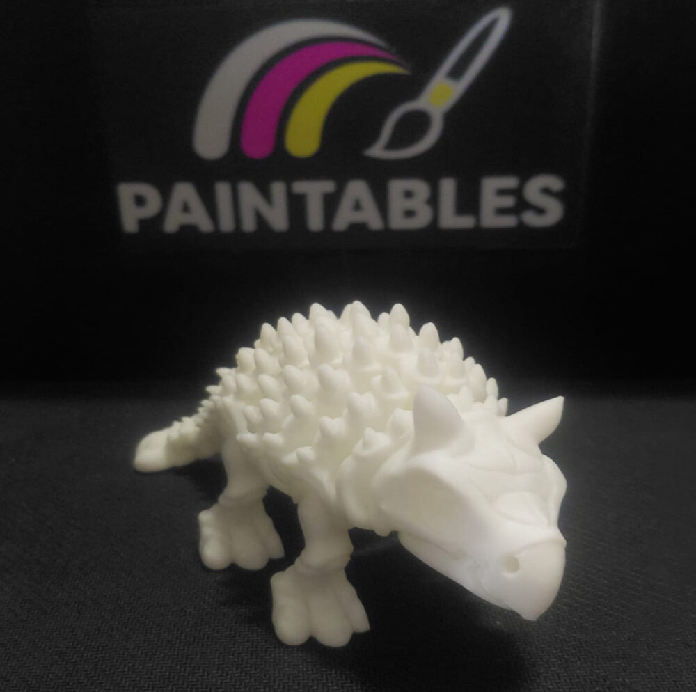 A front perspective view of a white 3D printed Ankylosaurus skeleton. The image highlights the dinosaur's skull, horns, and the rows of textured spikes leading down its articulated back.