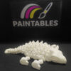 A white 3D printed Ankylosaurus skeleton lying flat in a resting pose. The view highlights the textured armored spikes along its back and the segmented articulated tail.