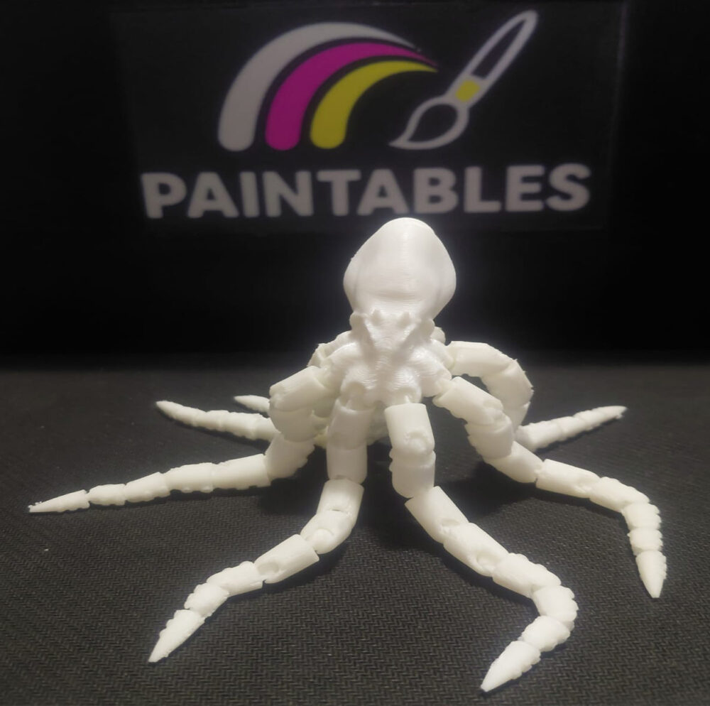 A white 3D printed articulated octopus model with its eight legs curved in various directions. The high-angle shot showcases the intricate joints of the tentacles and the smooth matte finish of the head, set against a black background.