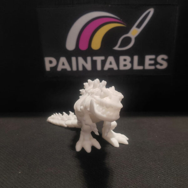 A head-on perspective of a white 3D printed Godzilla skeleton. The articulated model is shown in a forward-facing stance, highlighting its jagged dorsal fins, open jaw, and large three-toed feet.