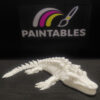 A white 3D printed Mosasaurus skeleton lying in a curved, swimming pose on a black surface. The model features a long, alligator-like skull with sharp teeth, four paddle-like flippers, and a segmented, flexible tail.