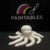 A white 3D printed articulated octopus named Ralph with a skull-shaped head. The model features eight thick, segmented, and highly flexible tentacles coiling outward on a black surface under a "Paintables" logo.