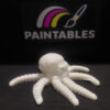 A side profile view of Ralph, a white 3D printed articulated octopus with a skull-shaped head. The model is shown on a black surface with its thick, segmented tentacles spread out, highlighting the intricate bone-like structure of the mantle.