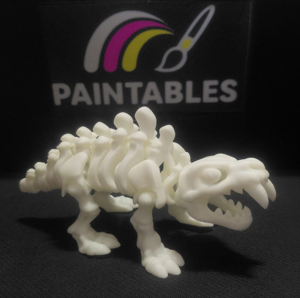 A side profile view of a white articulated 3D printed Sabertooth Tiger skeleton. The model is standing on a black surface, highlighting its curved spine, segmented ribs, and prominent saber-shaped fangs.