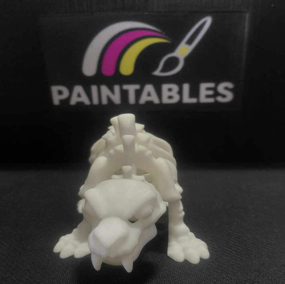 A front-facing perspective of a white 3D printed Sabertooth Tiger skeleton. The model is in a low prowling stance, showcasing the iconic long canine teeth, detailed skull, and wide paw structure.